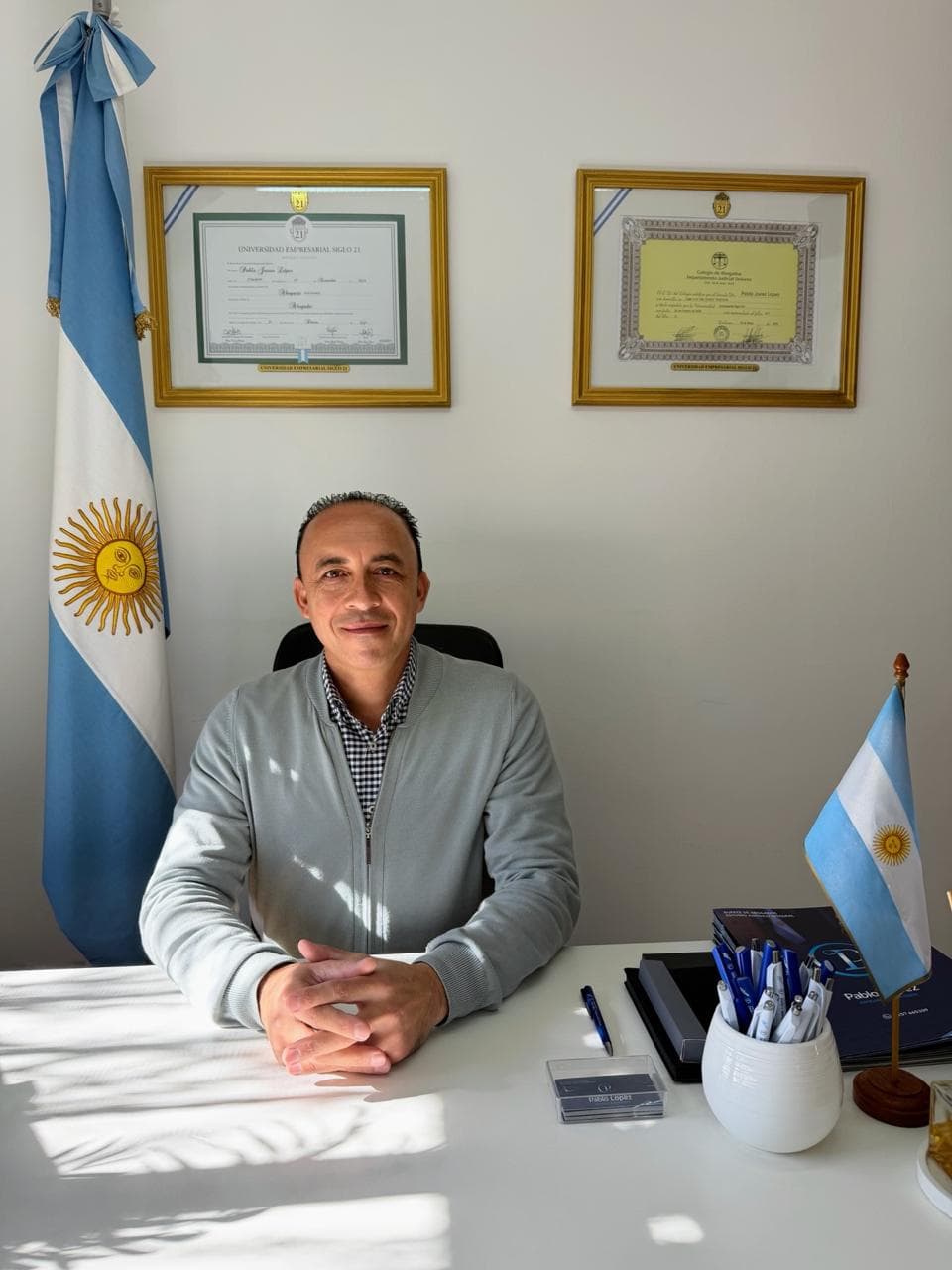 Dr. Pablo López sentado en su escritorio, con banderas argentinas de fondo